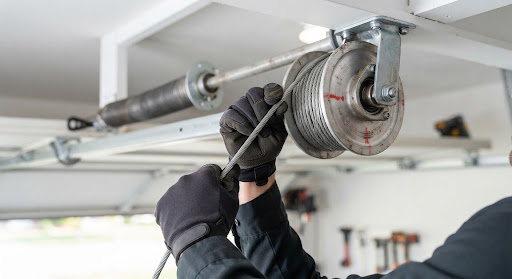Gloved hands guiding a lift cable onto the drum at the end of a garage door torsion shaft