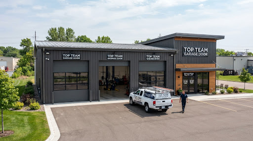 Dark steel shop building with three tall sectional garage doors with window sections and a service pickup parked in front